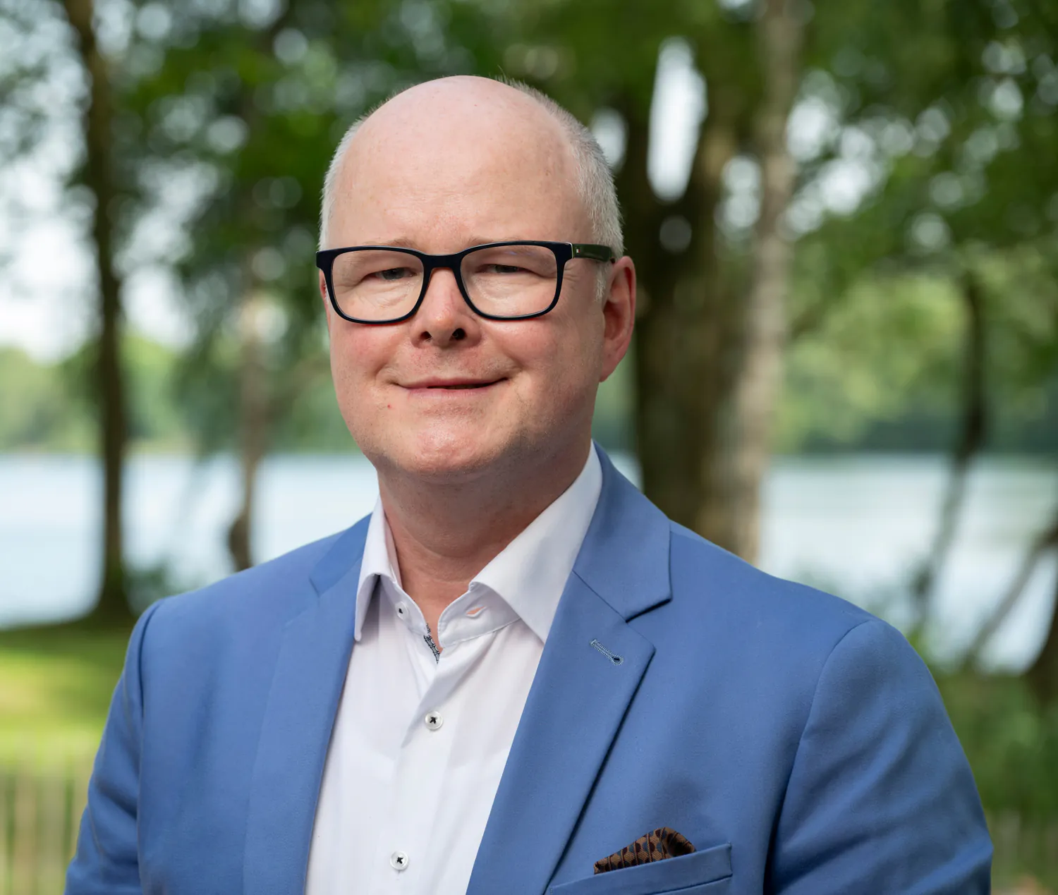 Nahaufnahme von Thomas Spieker im blauen Sakko vor Bäumen und Wasser